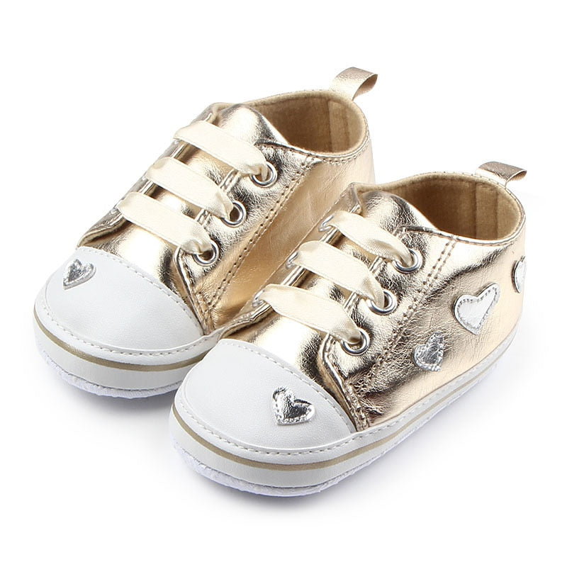 Shiny little golden sneakers for your baby girl age newborn to 18-months-old. Upper Material: PU. Outsole Material: Cotton. Closure Type: Lace-up. These sneakers comes in red, pink, black and gold.